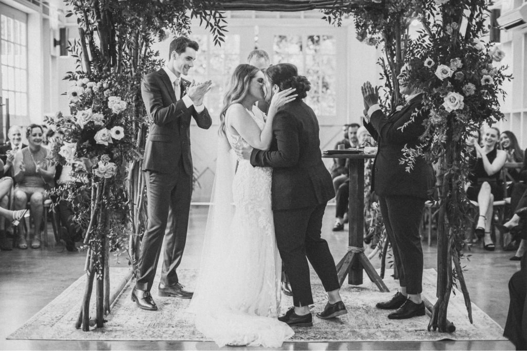 black and white photo of two brides kissing at the alter at The Lombardi House in Los Angeles at the end of their ceremony and everyone excited for them