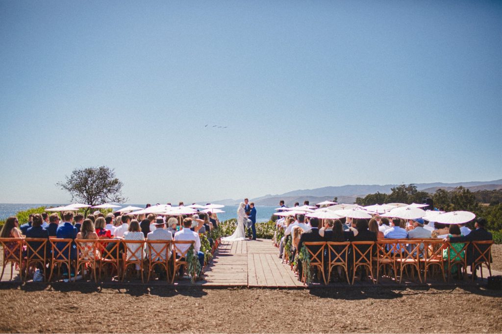 Photo of the wedding Ceremony at Dos Pueblos Orchid farm over looking the bluffs with all of the congregation and the wedding couple in the photo