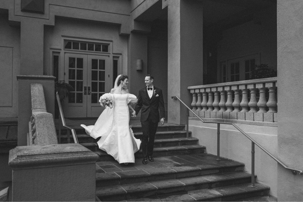 classic black and white photograph of the bride and groom walking down the grand staircase to their cocktail hour at the Ritz Carlton Marina Del Rey