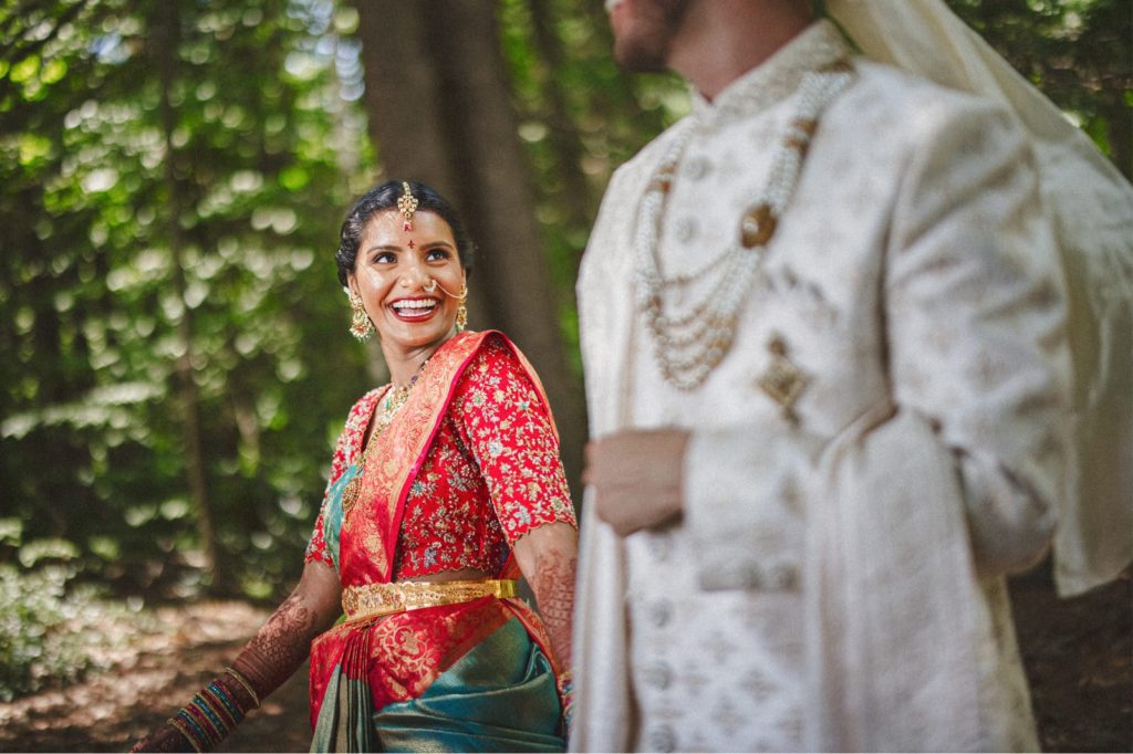Bride smiling at her groom in traditional indian colorful sari as they walk out of the woods at the Valley View Farm wedding venue
