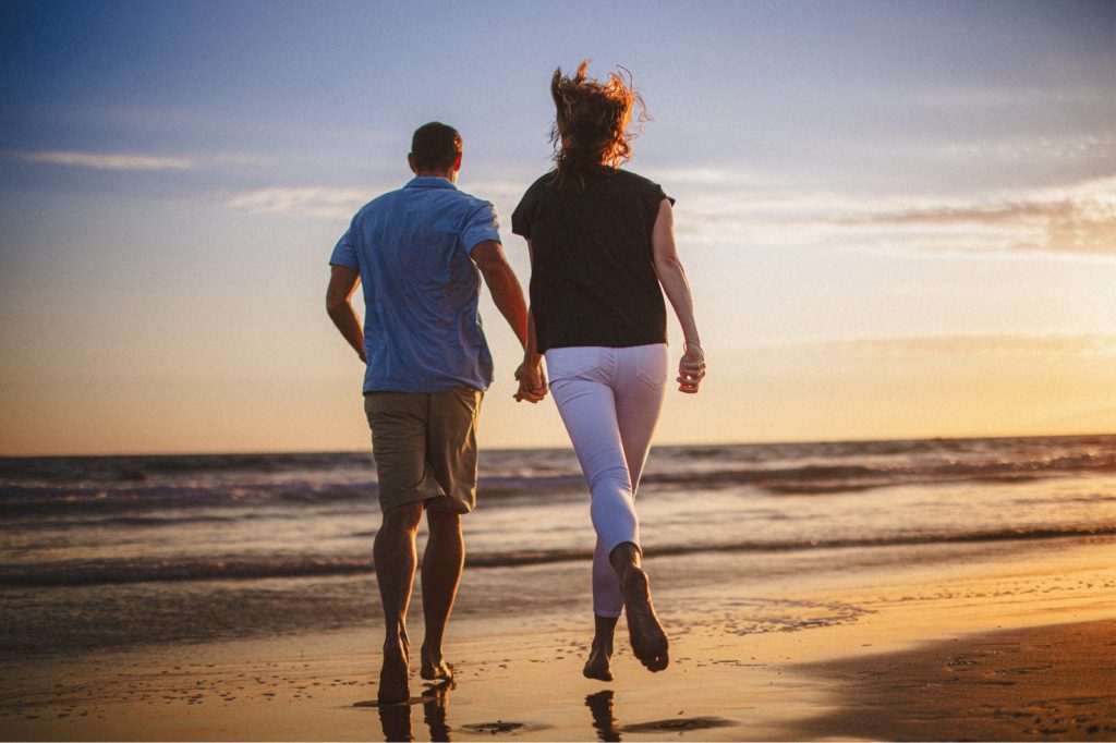 Couple running holding hands at Santa Monica beach engagement session