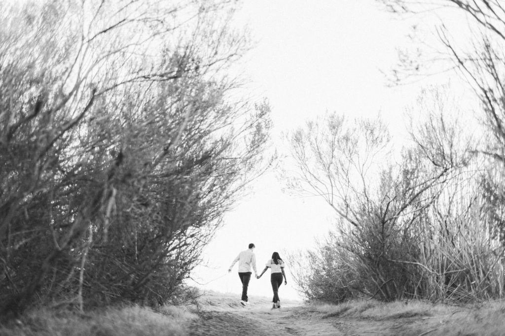 A creative engagement photo of The bride and groom walking away taken through bushes in a black-and-white photo at the Santa Barbara butterfly preserve in Goleta California