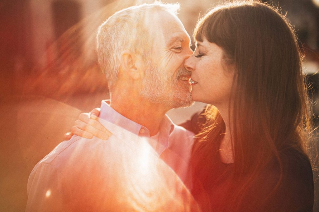 Warm and romantic couples portrait on Main Street in downtown Ventura with the light coming in from the top and creating dramatic Sunflare while they kiss